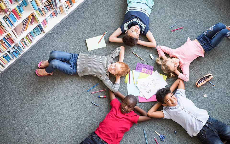 Photo d'illustration présentant des enfants allongés au sol devant leurs dessins.